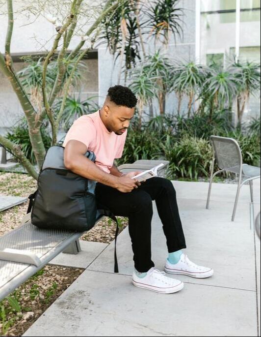 A Black, male student sits on a bench, reading a book.